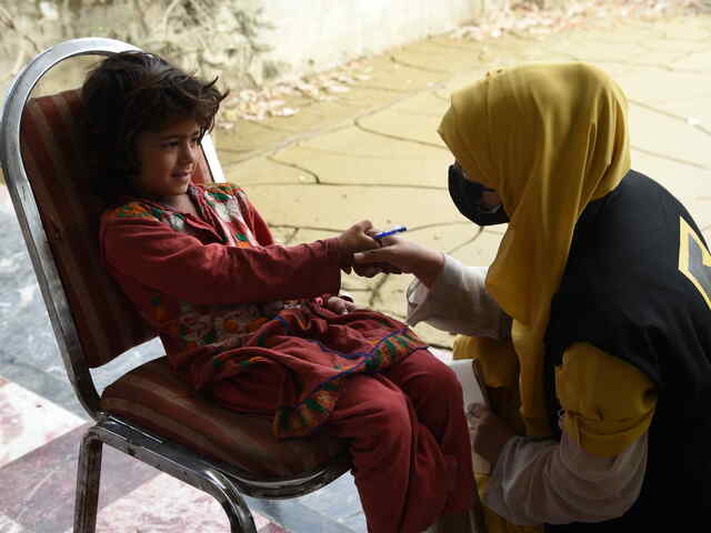 A young girl sits in a chair and smiles while shaking hands with an IRC staff member.